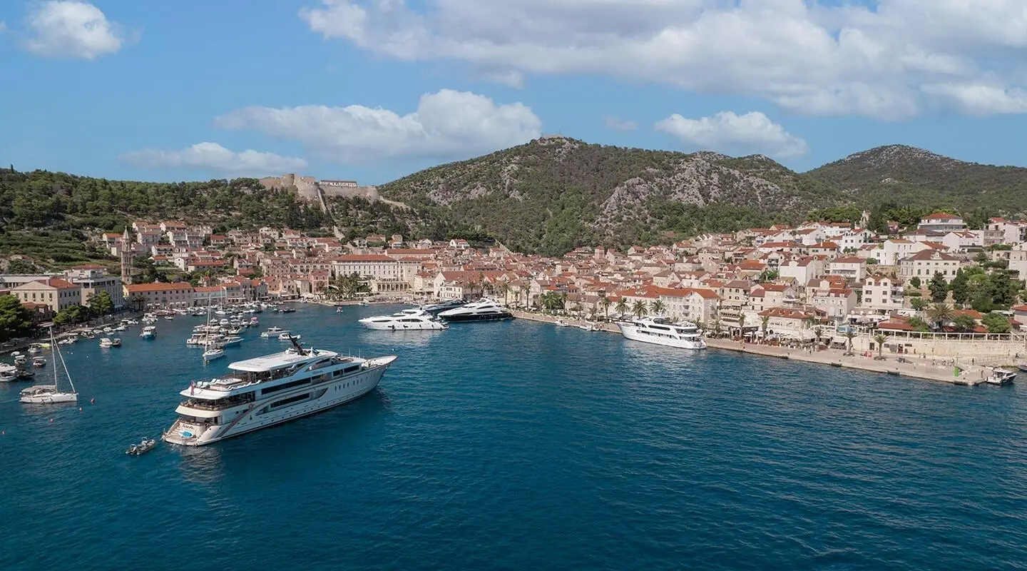 Riva motor yacht anchored in a coastal bay with clear blue water and town on hills