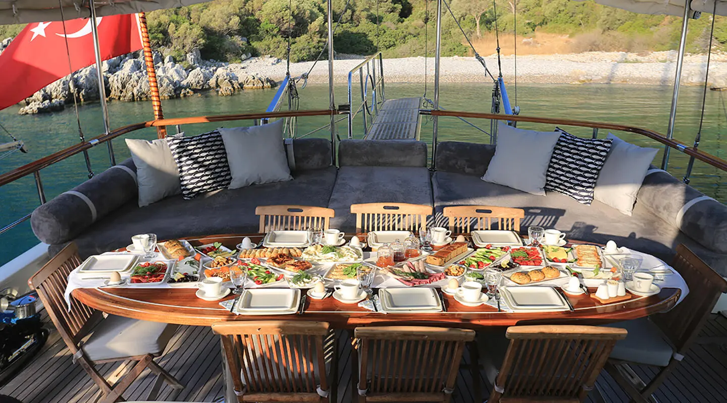Grand Sailor yacht charters table set with plates and glasses on deck at sunset