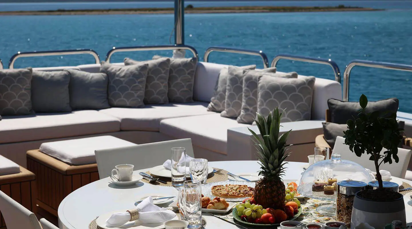 Alalya yacht dining setup on deck with plates, glasses, and pineapple centerpiece