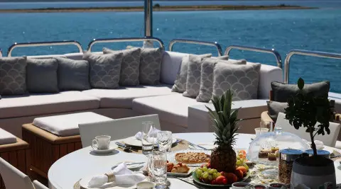 Alalya yacht dining setup on deck with plates, glasses, and pineapple centerpiece