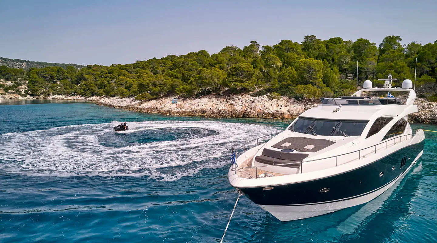 M Five luxury yacht anchored near rocky coastline with evergreen trees, clear blue water