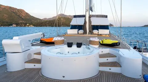View of a white circular seating area on a yacht with masts and sunset in the background