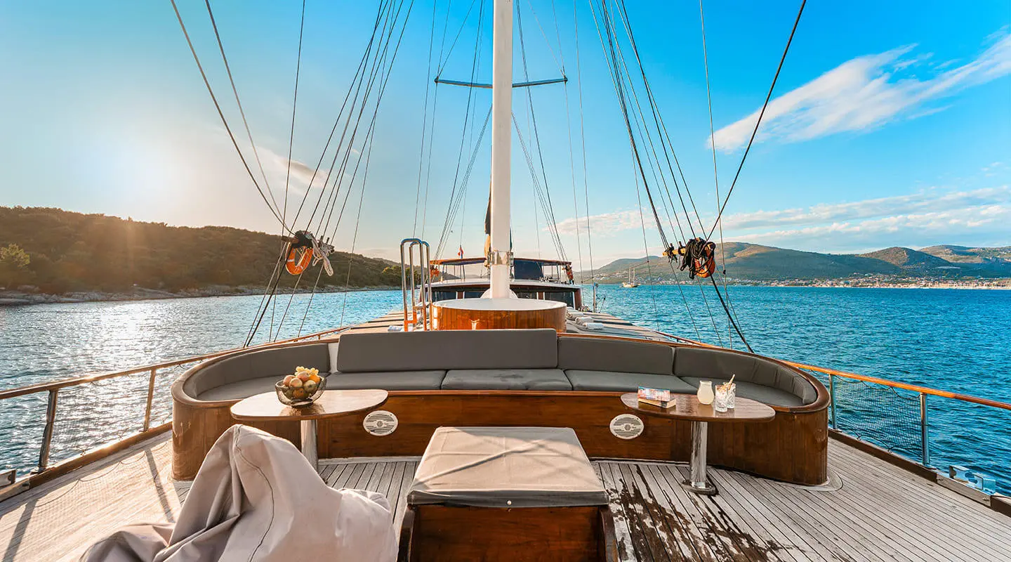 Deck view of a yacht with wooden helm, sails, and blue sea ahead