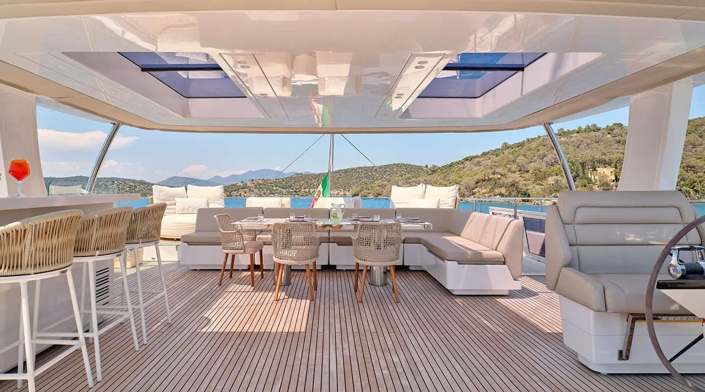 Yacht Genny aft deck with seating, table, and shaded sun loungers under a blue sky