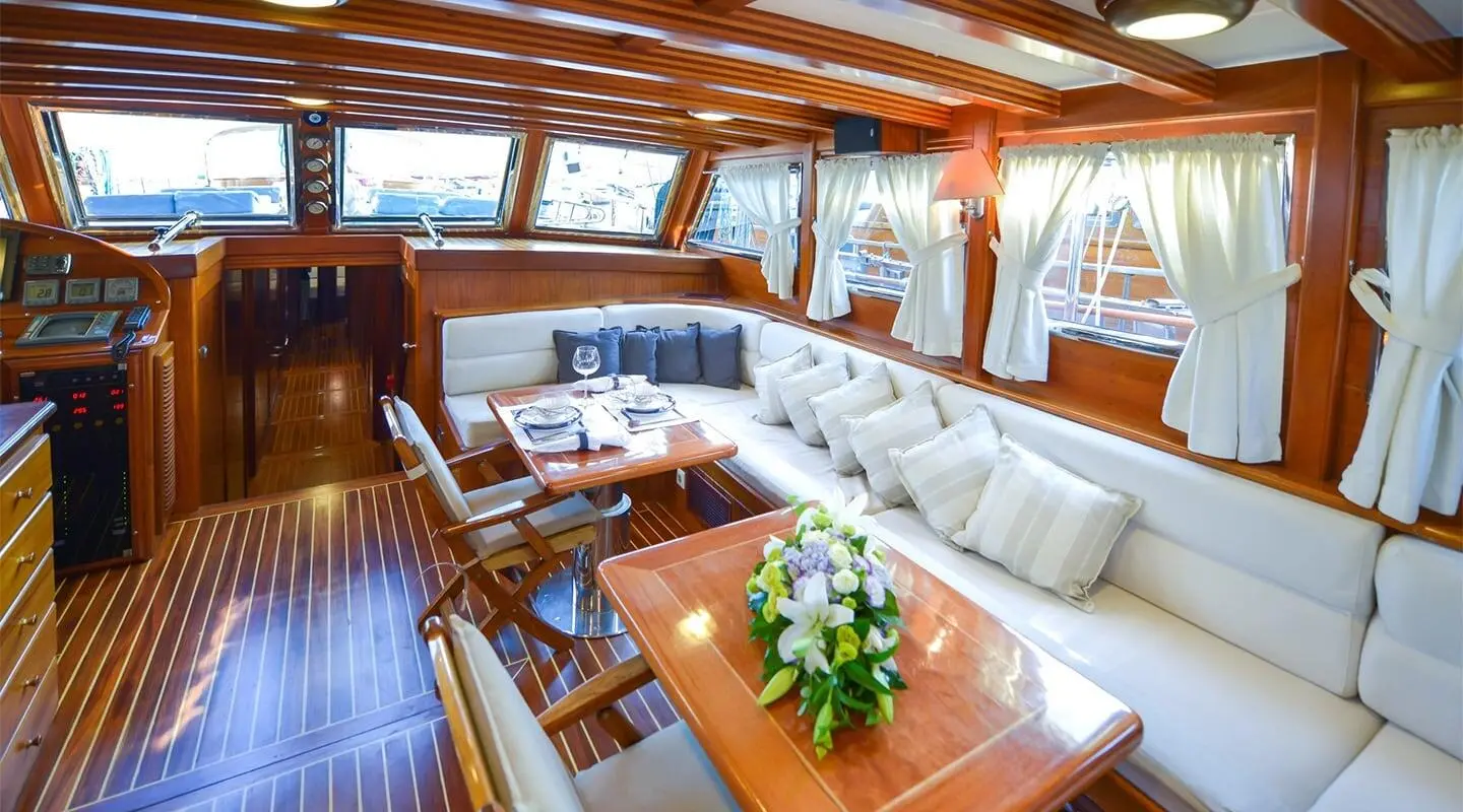 Ros Mare yacht interior with beige seating, wooden table, and sunset light