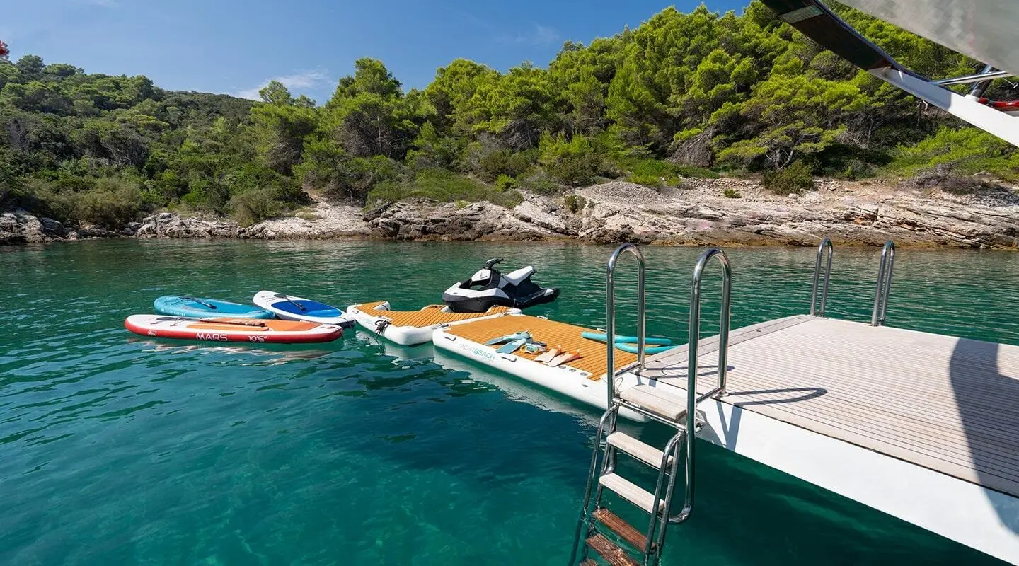 Yacht with turquoise water, a dock, and multiple water sport boards and a jet ski nearby