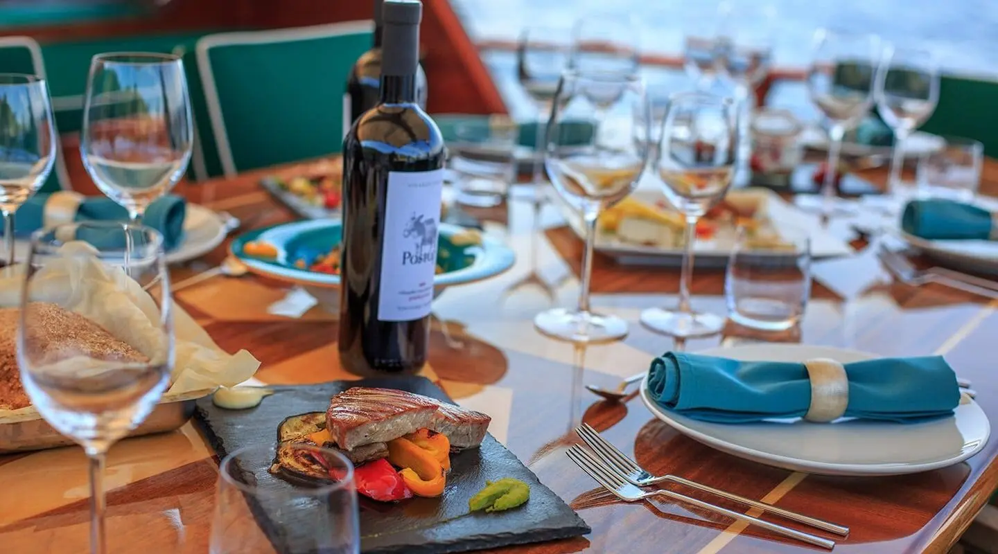 Table set on deck with wine bottle, wine glasses, bread, and plated food on a yacht