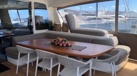 Outdoor deck with central wooden table and seating, wicker chairs around, flower arrangement on the table, and glass and deck surroundings