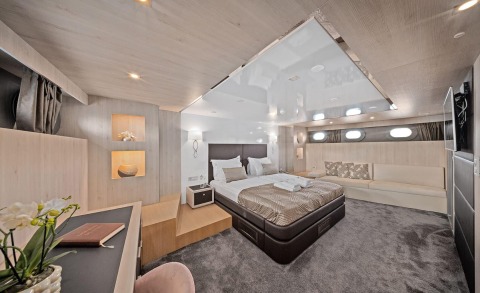 Bedroom interior with large bed, upholstered headboard, side tables, seating area and warm wood panel walls