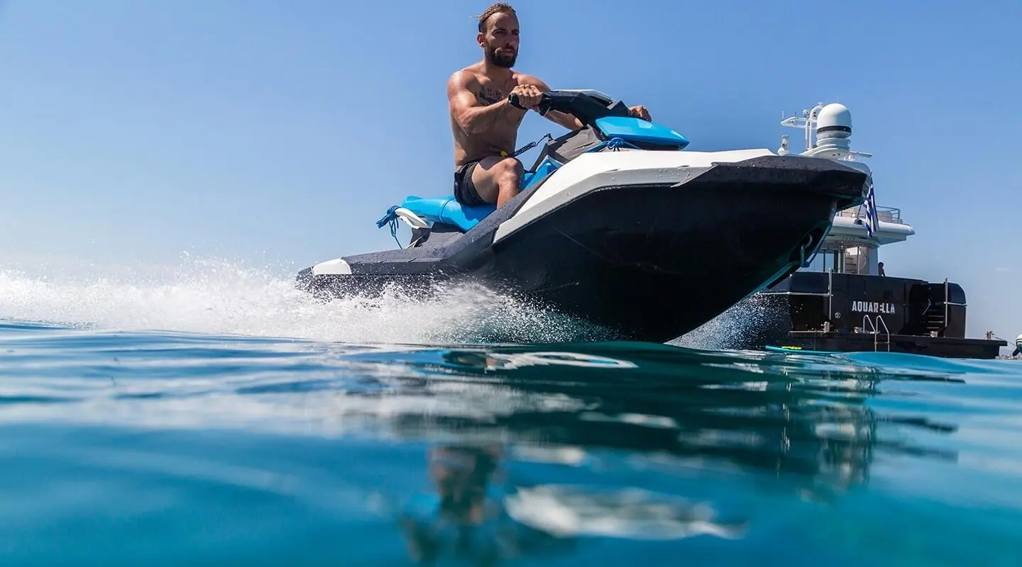 Man riding a blue jet ski on the bow of a motor yacht