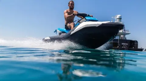 Man riding a blue jet ski on the bow of a motor yacht