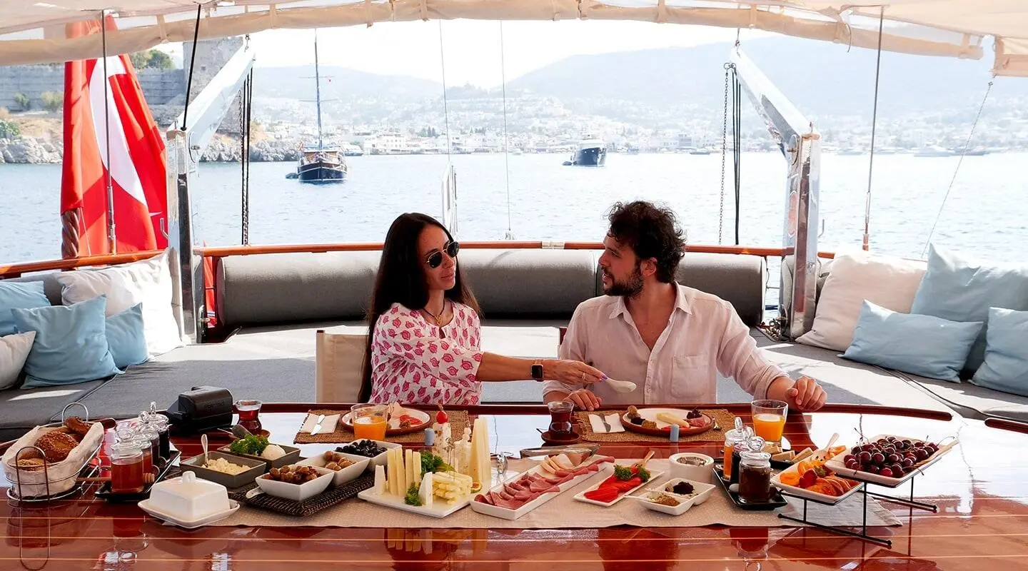 Two people dining at a sunset yacht deck with plates and drinks