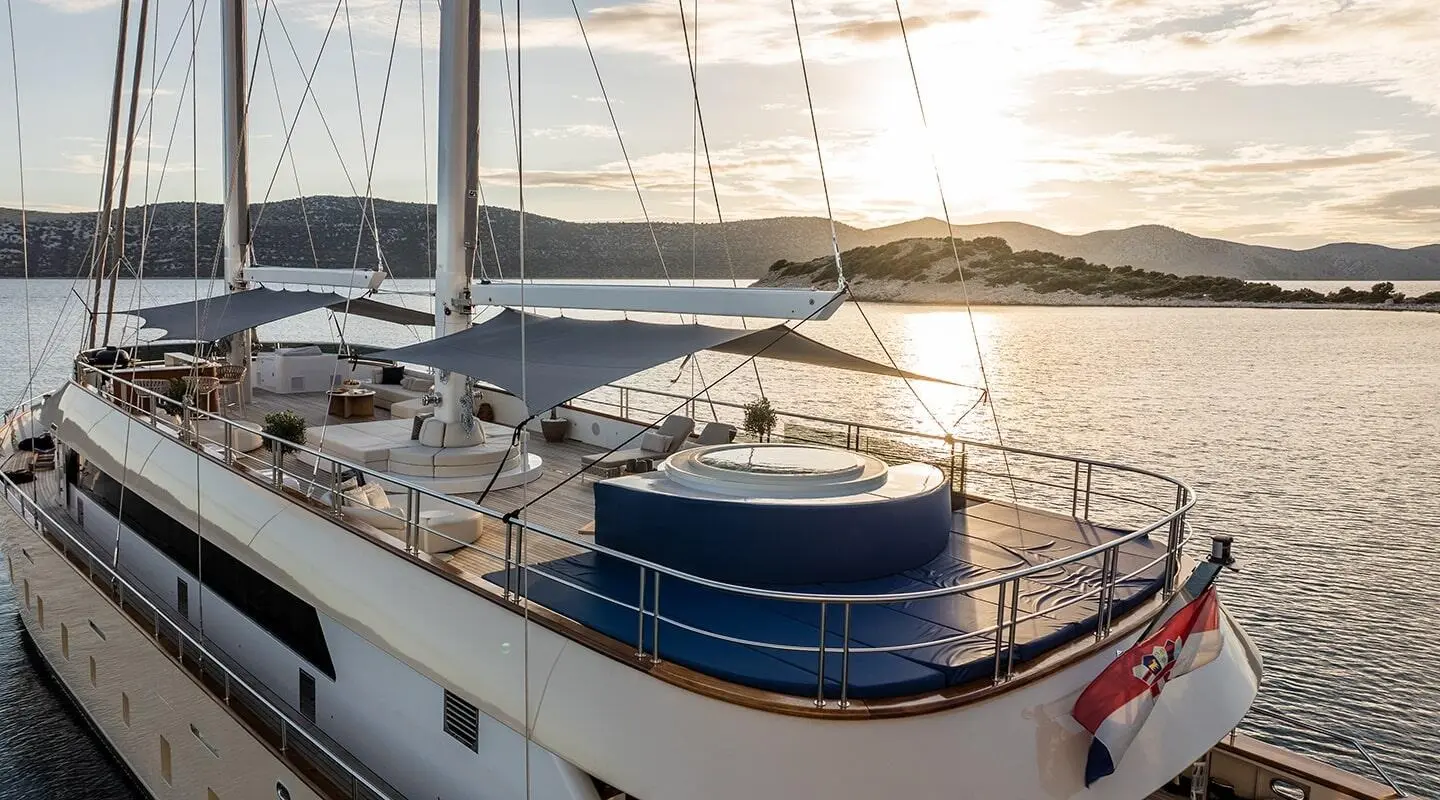 Maxita yacht deck scene with sunlit railing, blue fender, and sails in view