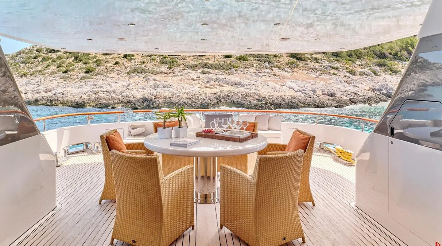 Mobius luxury motor yacht dining area with table set for guests on deck, sea shore in background
