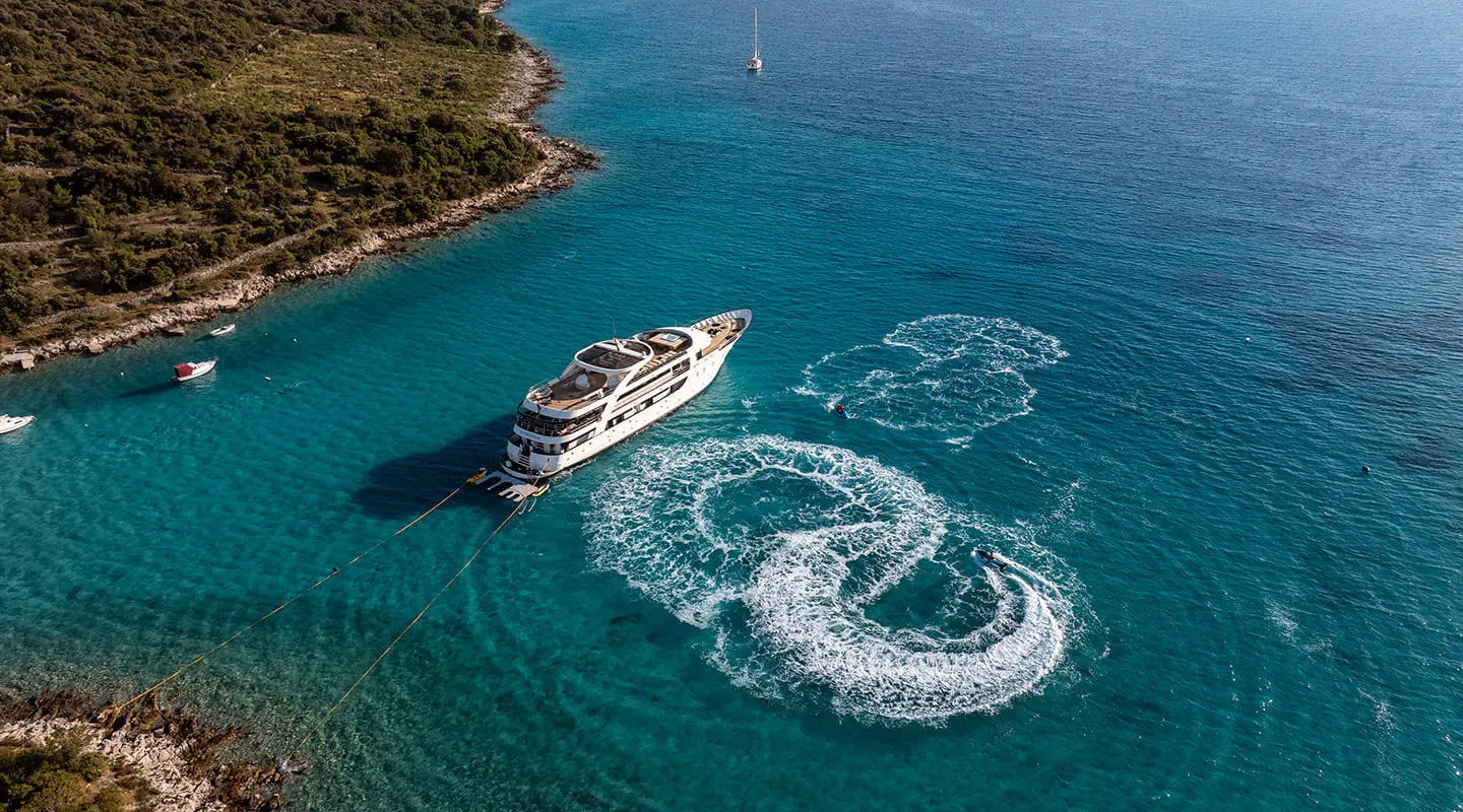 A sleek motor yacht named Karizma sails near rocky coastline with a smaller boat nearby