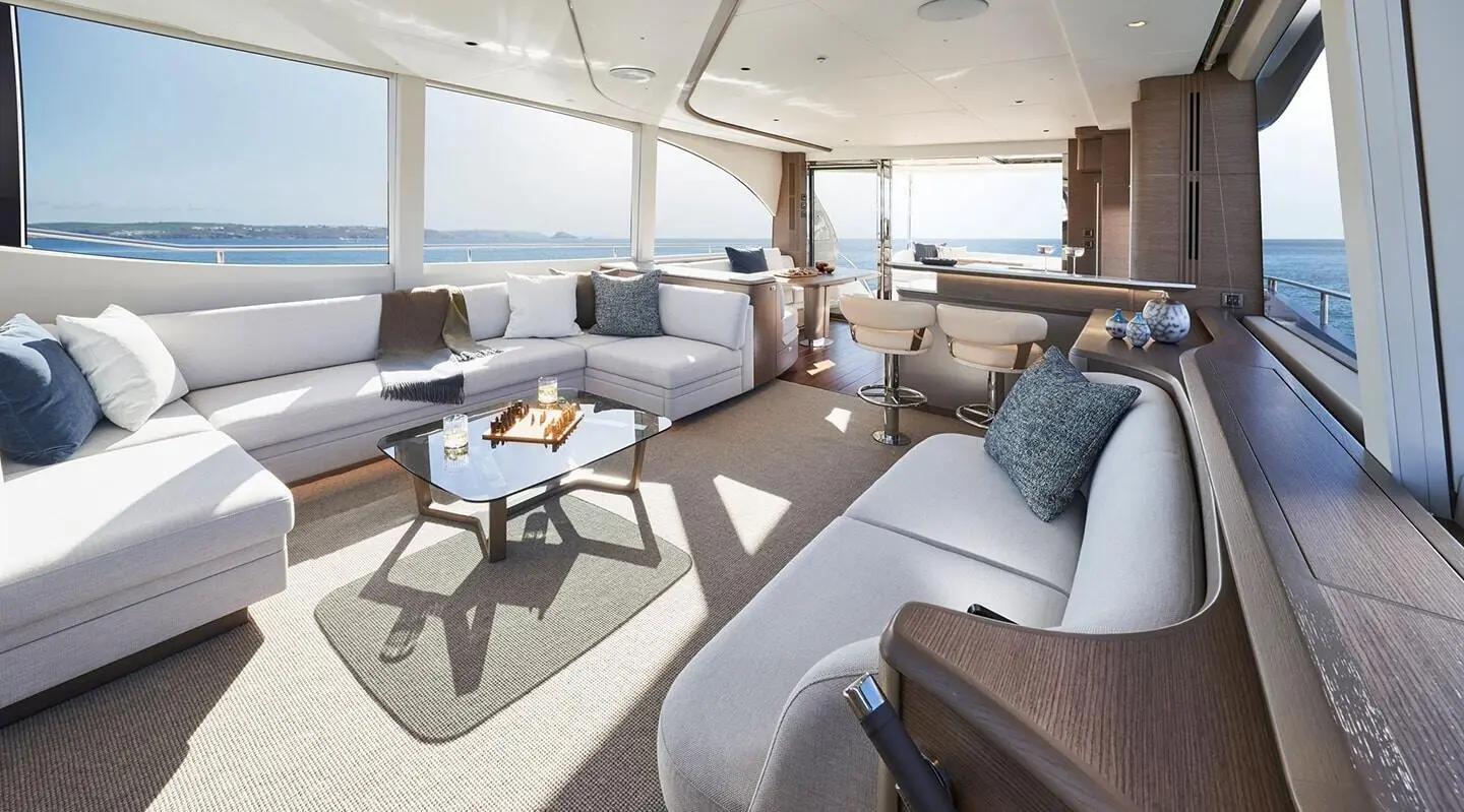 Spacious yacht saloon with light cushions, wood accents, and large windows
