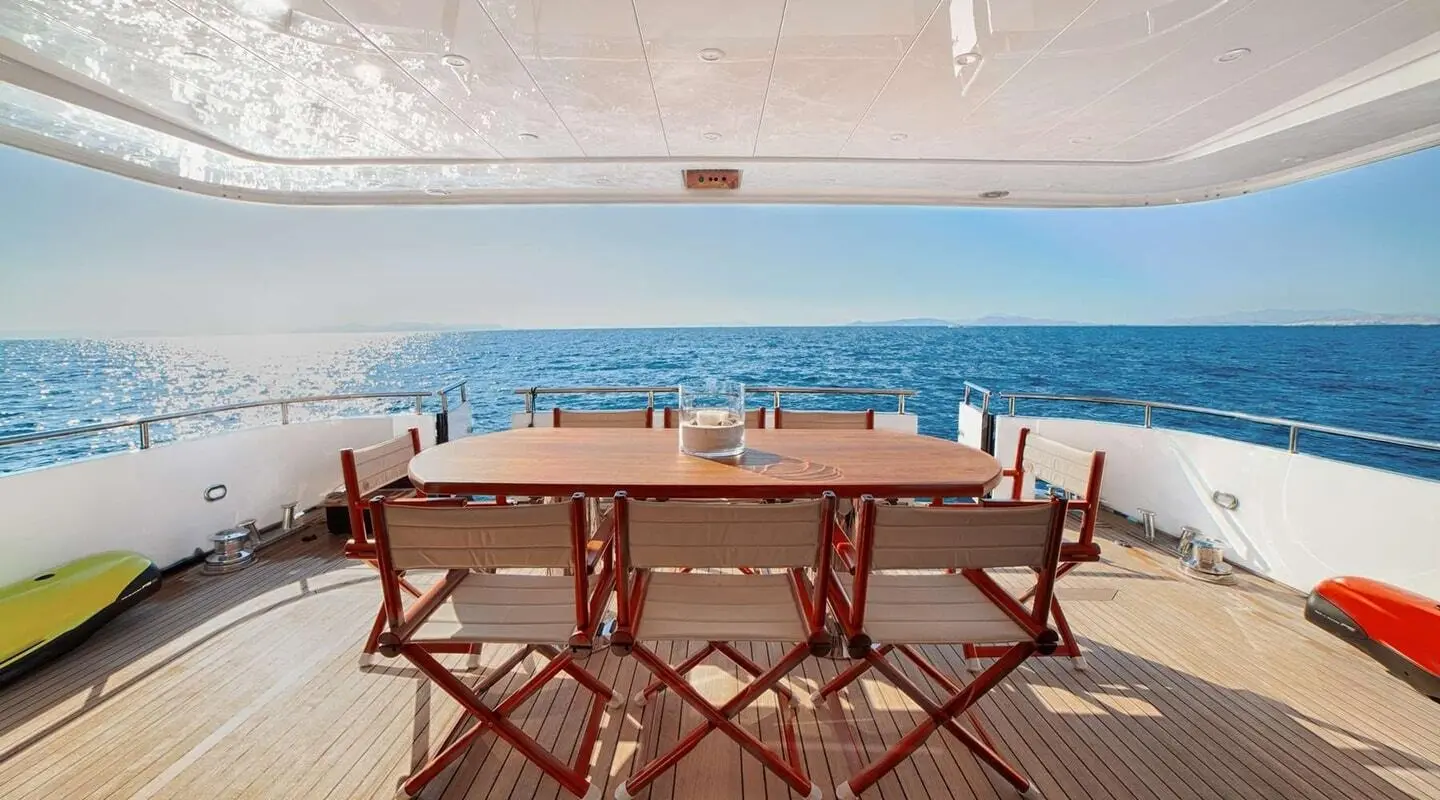 Yacht Zoi deck dining area with long wooden table and chairs overlooking the sea