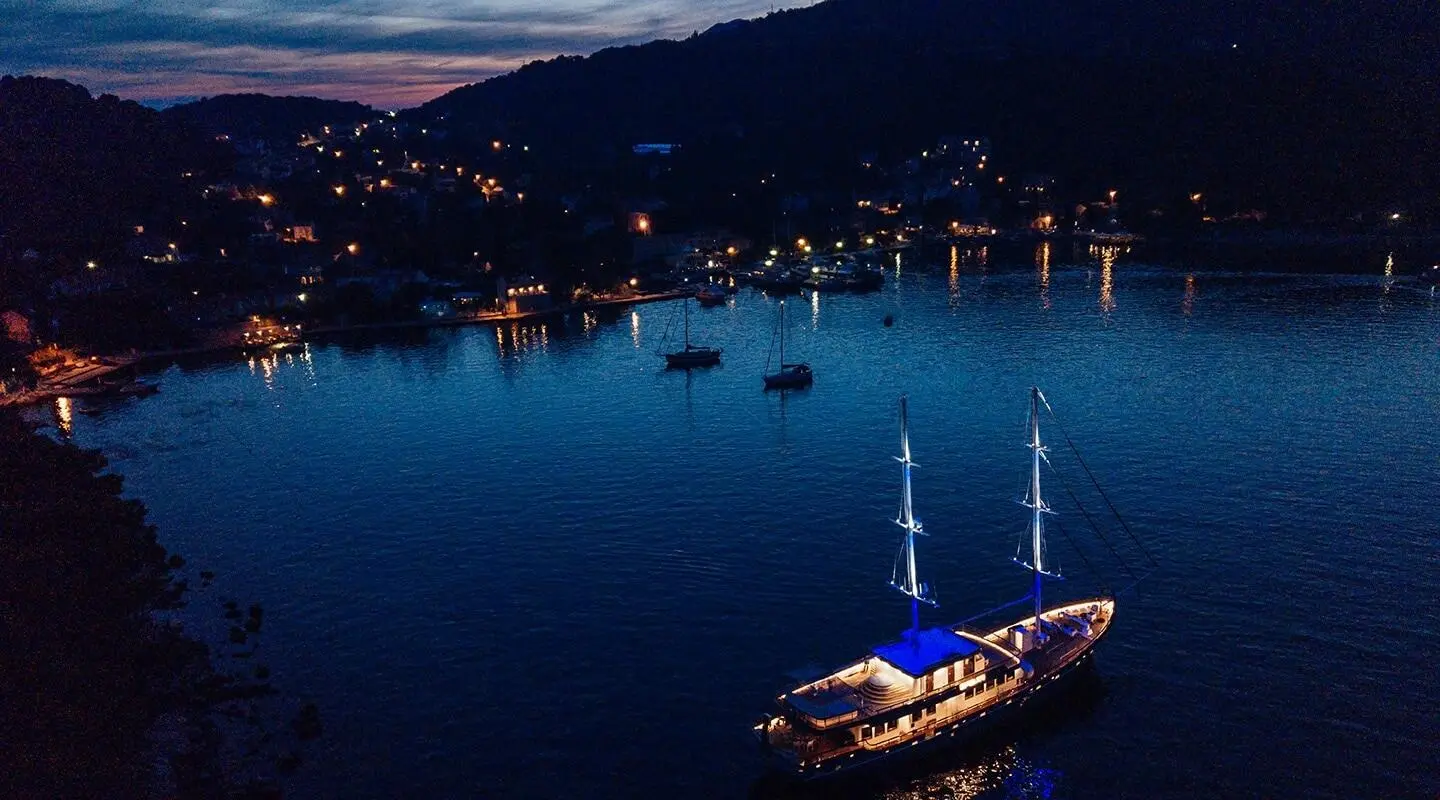 Corsario luxury gulet at night calm sea with lit harbor lights nearby