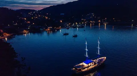 Corsario luxury gulet at night calm sea with lit harbor lights nearby