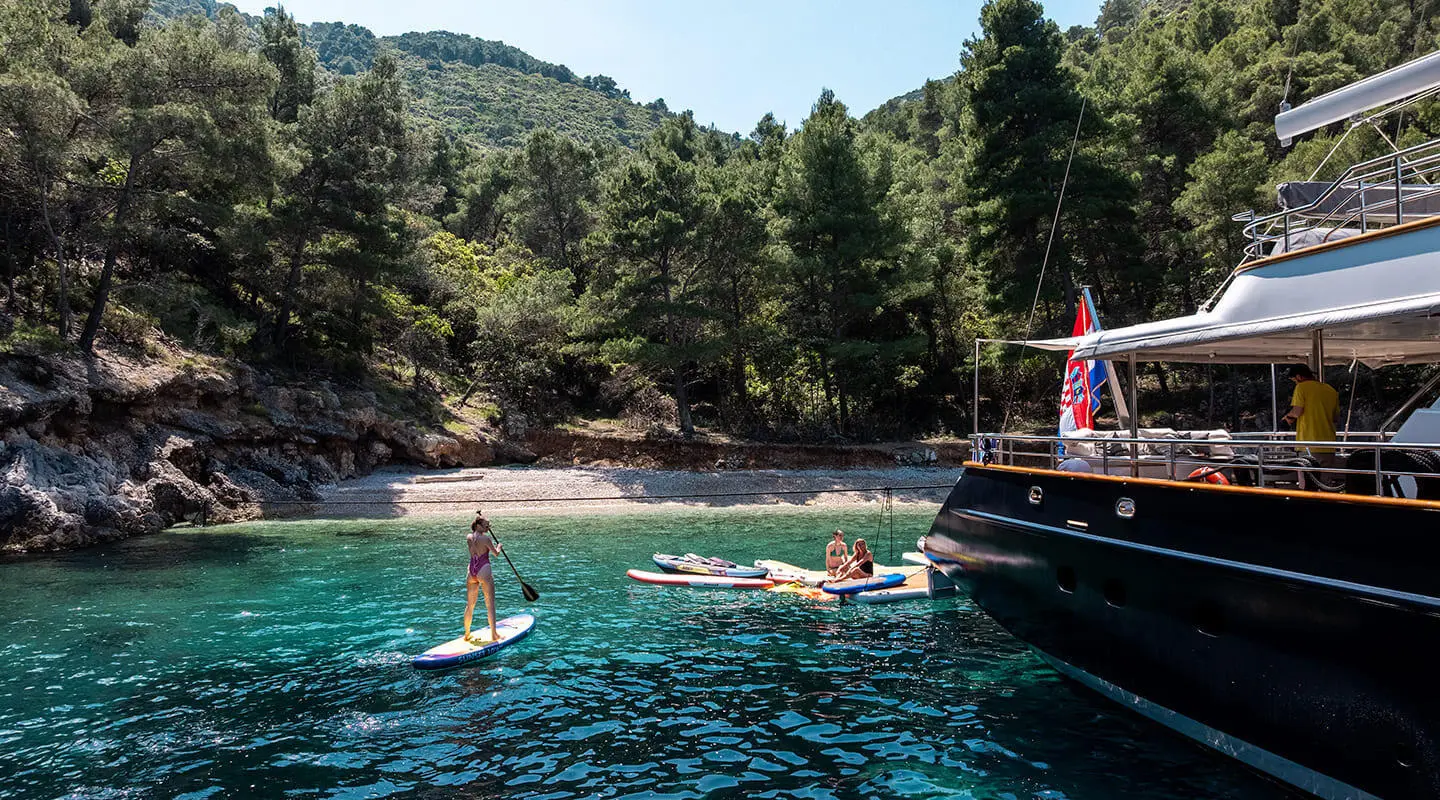 Dalmatino yacht anchored near a rocky shore with people swimming nearby
