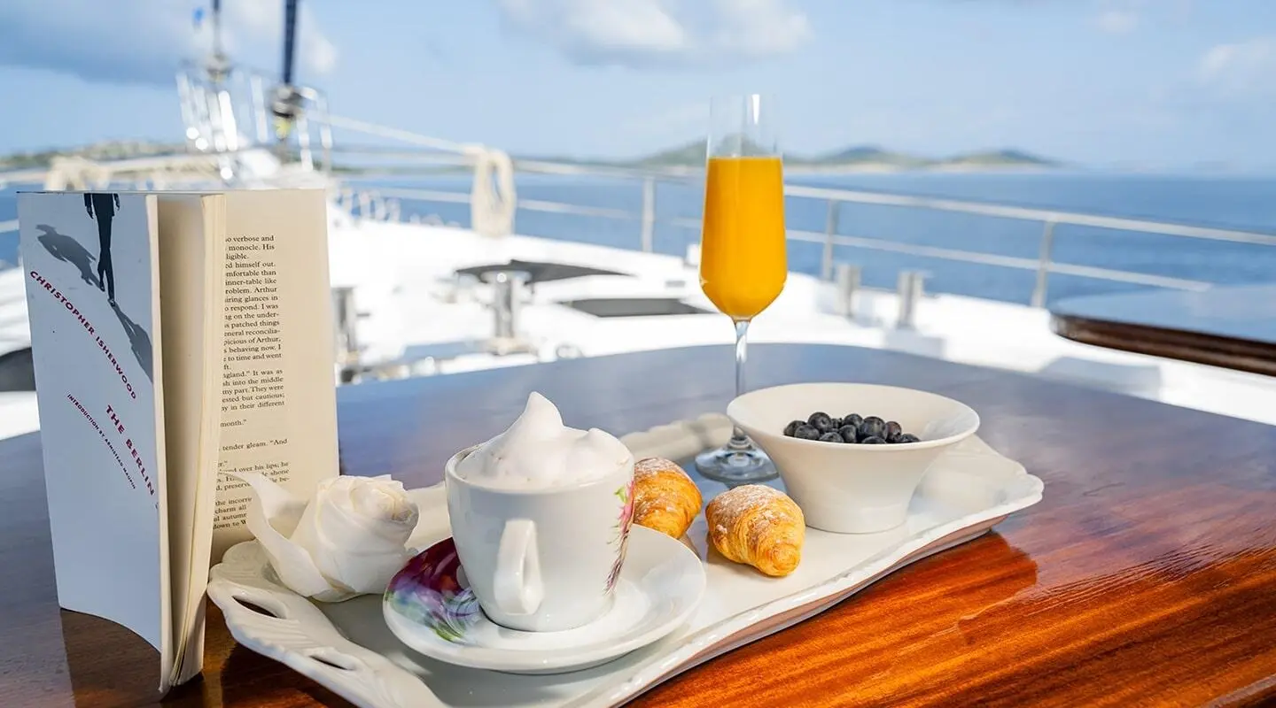 A deck table set for two on a luxury yacht with white chairs and ocean view at sunset