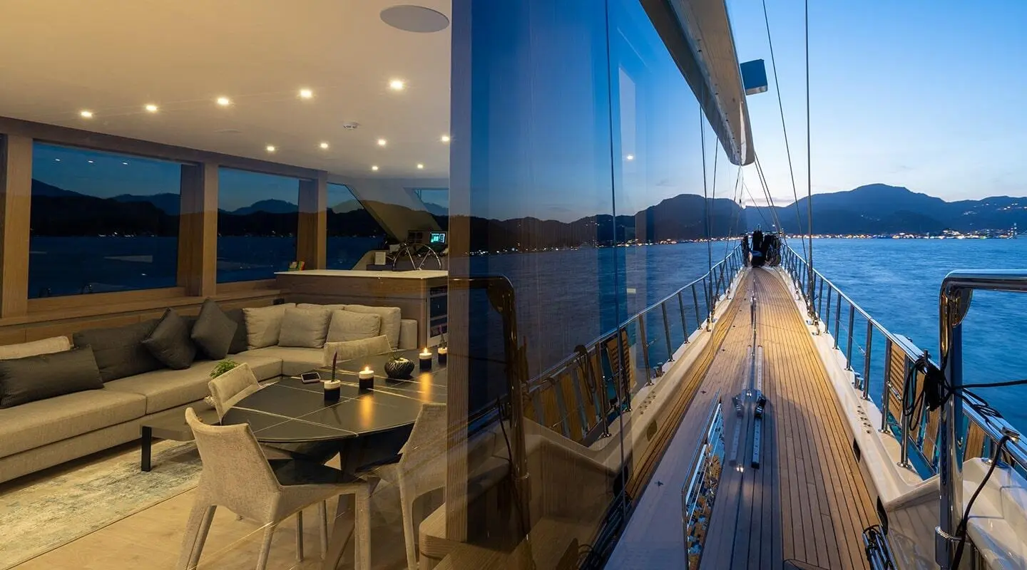 Side deck of the Good Life yacht with glass windows, outdoor seating, and blue water view