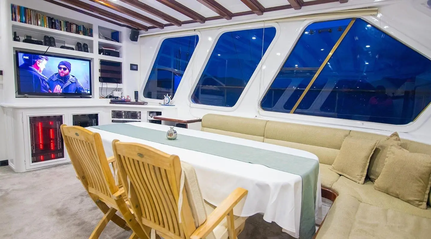 Gulet Grande Mare interior with dining table and wooden chairs by cabin windows