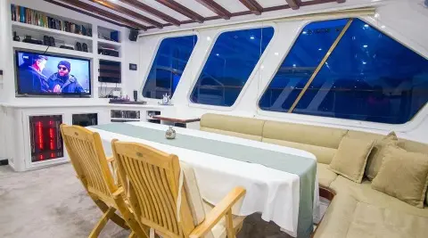 Gulet Grande Mare interior with dining table and wooden chairs by cabin windows