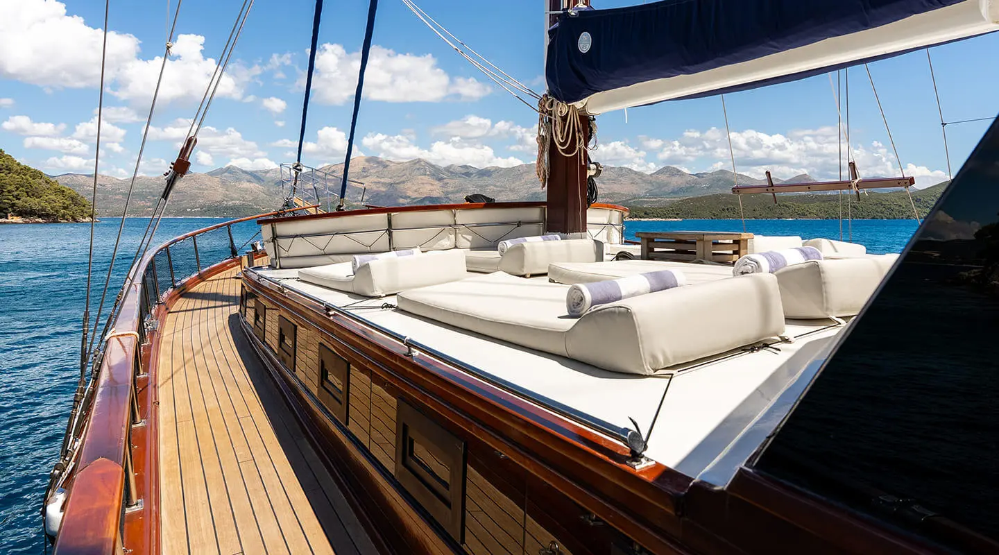 Eleganza yacht deck with polished wooden railing, white seating, and blue sea horizon at sunset