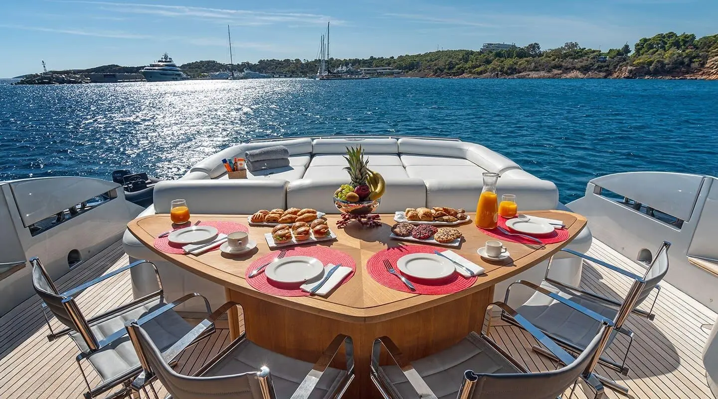 Sunset-lit yacht dining table set with red plates and wine on deck