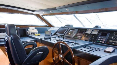 Grace yacht helm cockpit with wooden wheel and navigation screens on blue console