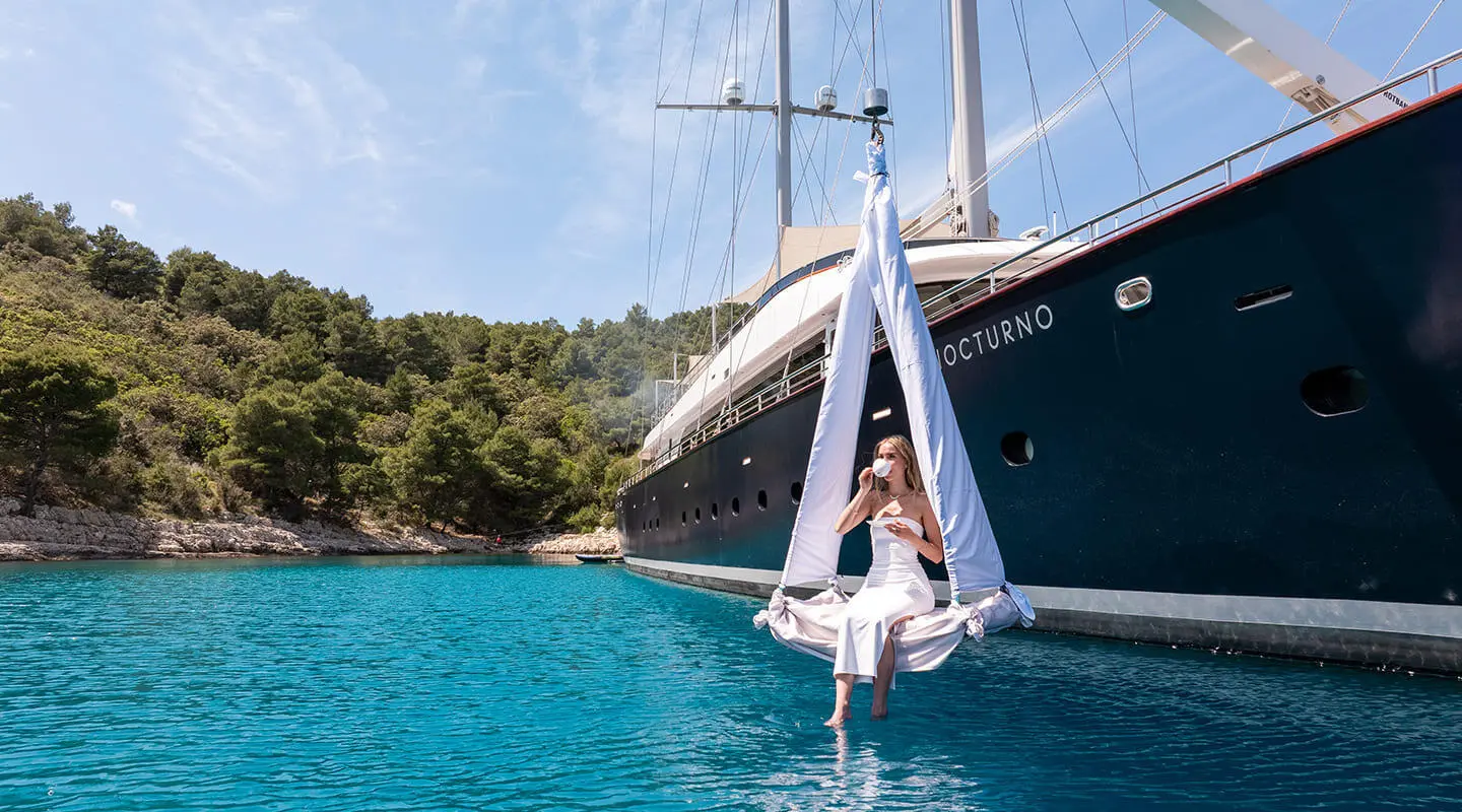 Nocturno yacht anchored near turquoise water with a white sailboat, coastal trees