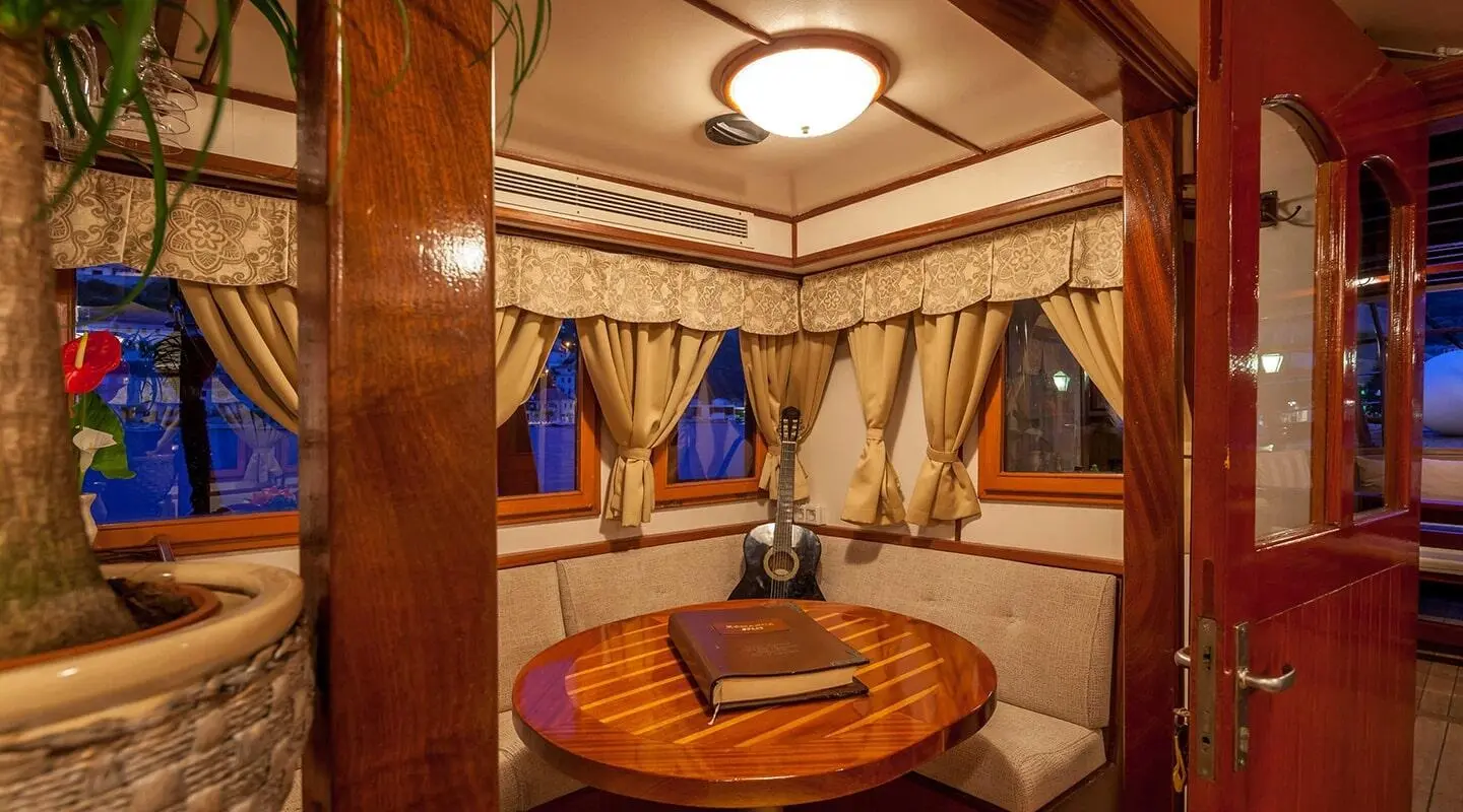 Romanca yacht interior with circular wooden table and blue curtains at sunset