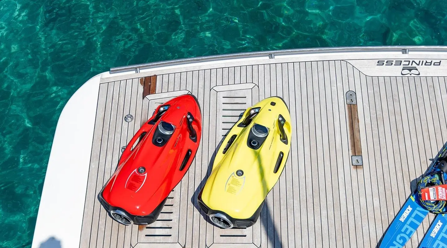 Red and yellow jet skis on a yacht deck with turquoise water nearby