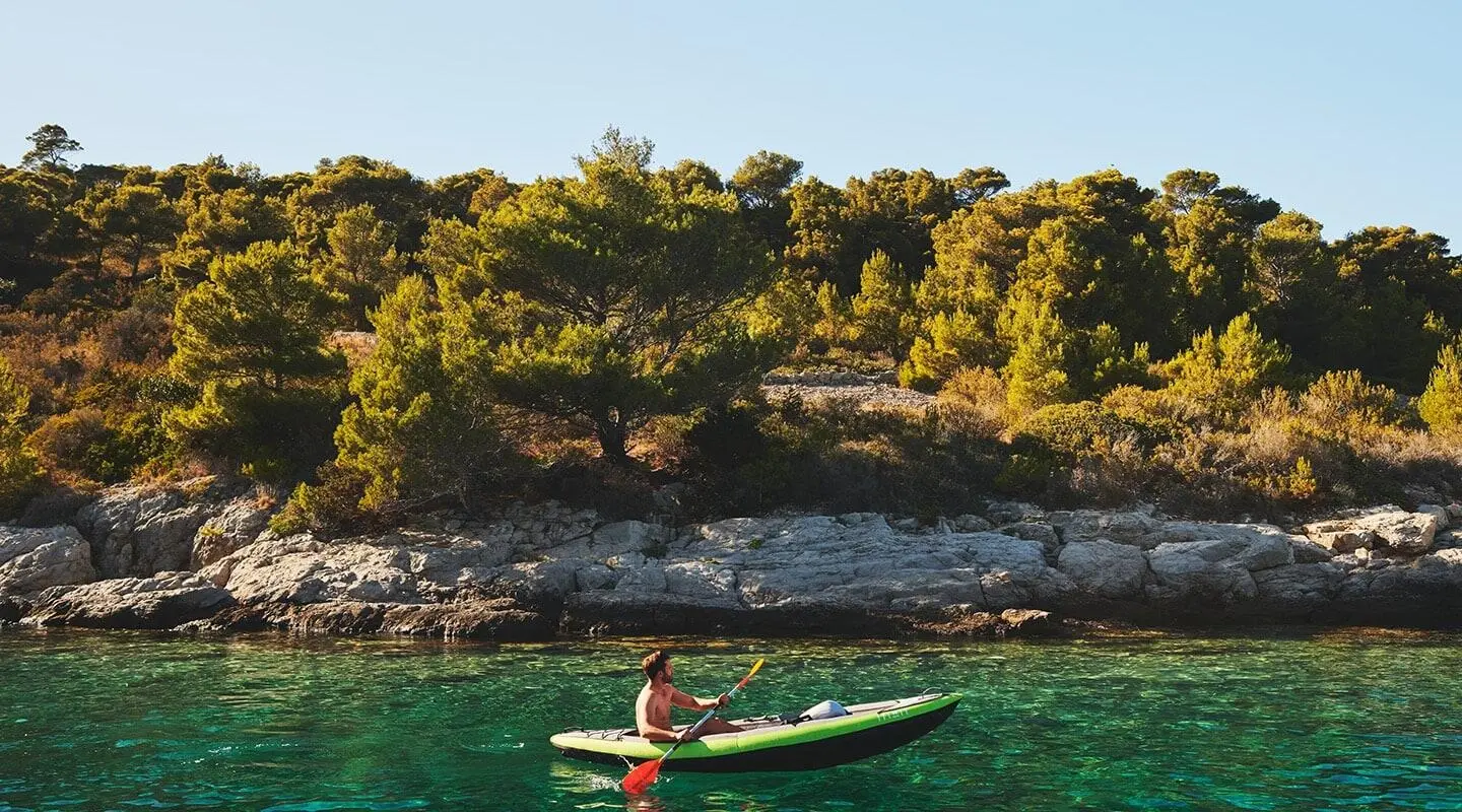 Corsario yacht anchored near rocky coastline with a small kayak in turquoise water