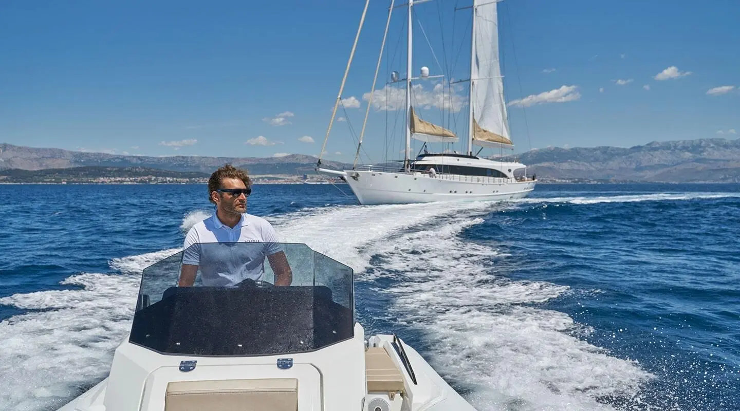 Yacht Acapella cutting through blue sea at sunrise with deck crew on bow