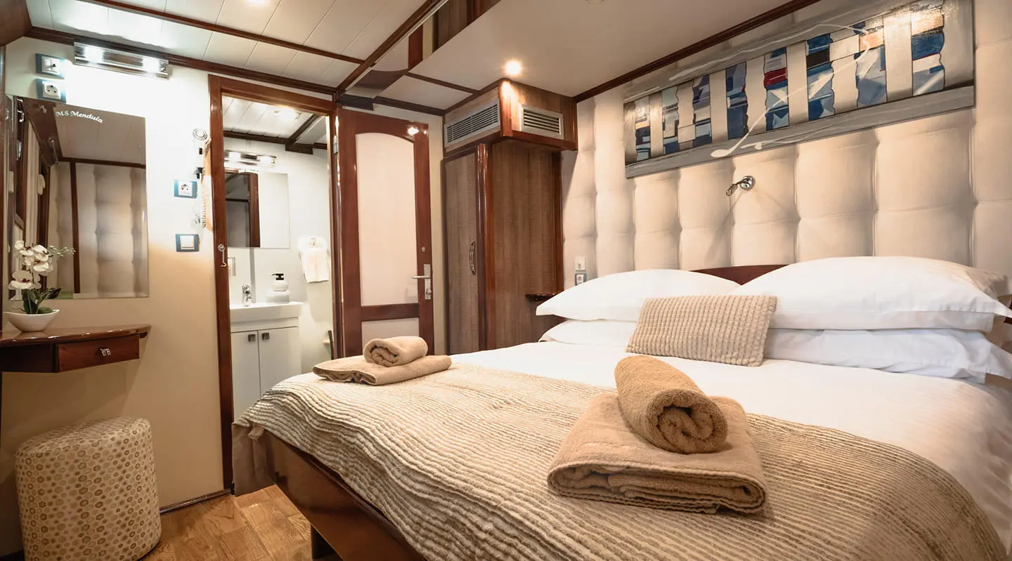 Mendula yacht interior with a large bed, pillows, and wooden cabinetry at sunset