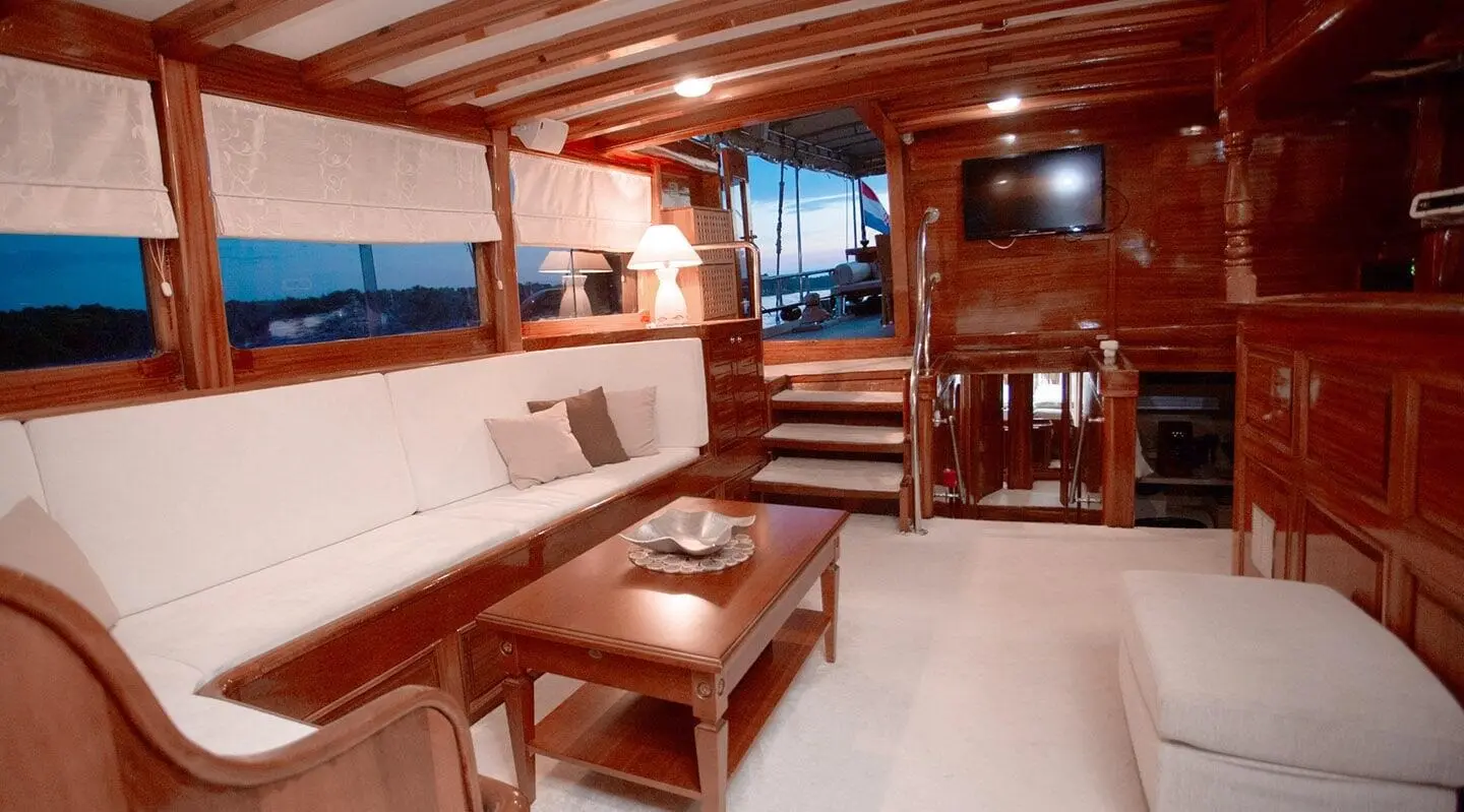 Malena yacht interior with wooden paneling, seating area, and windows showing sunset