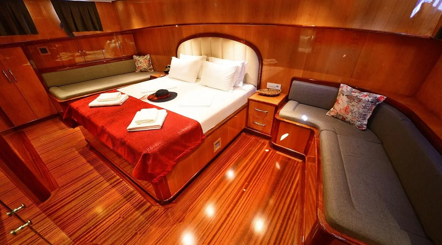 Maya luxury gulet interior with polished wood, bed, red blanket, pillows