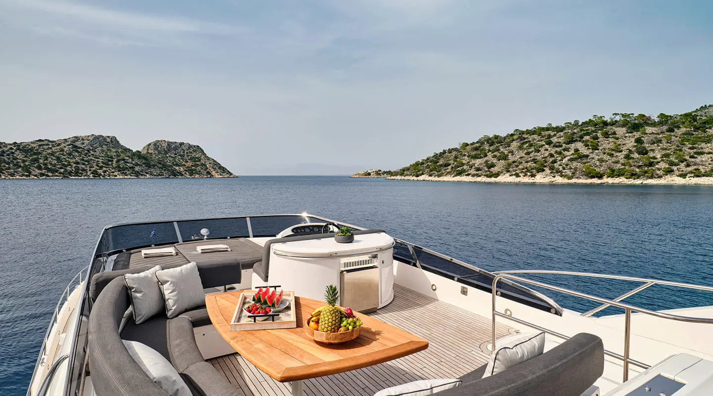 Luxurious yacht deck with curved seating, cushions, and a wooden table on a clear blue sea