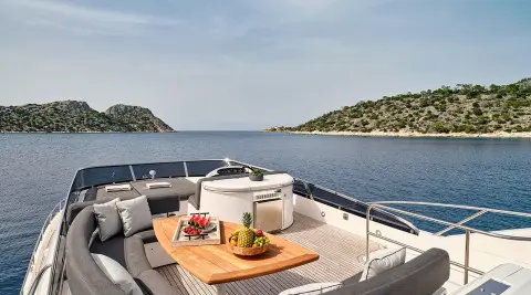 Luxurious yacht deck with curved seating, cushions, and a wooden table on a clear blue sea