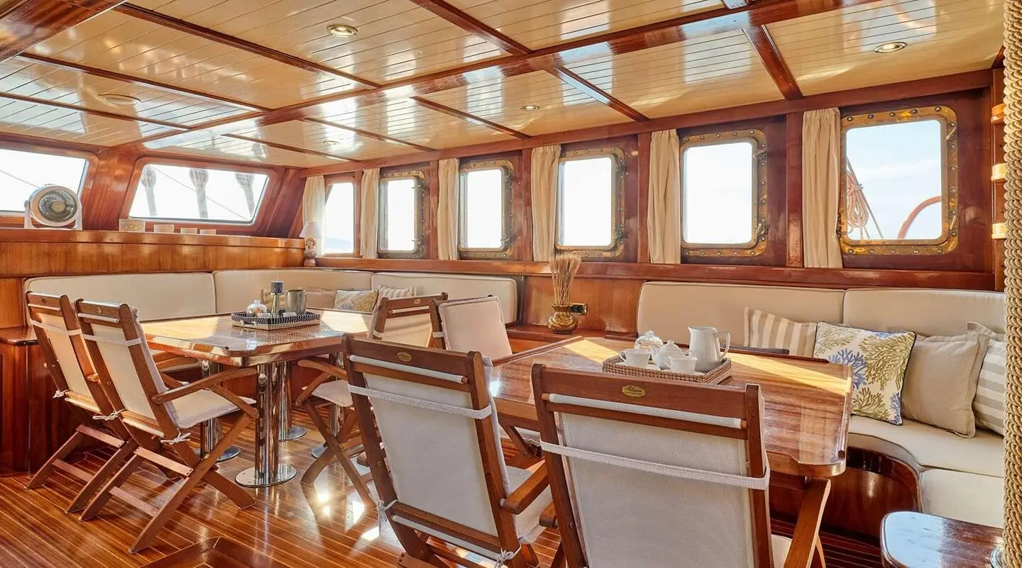 Myra yacht interior with wooden tables, chairs, and windows on a sunny day