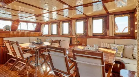 Myra yacht interior with wooden tables, chairs, and windows on a sunny day