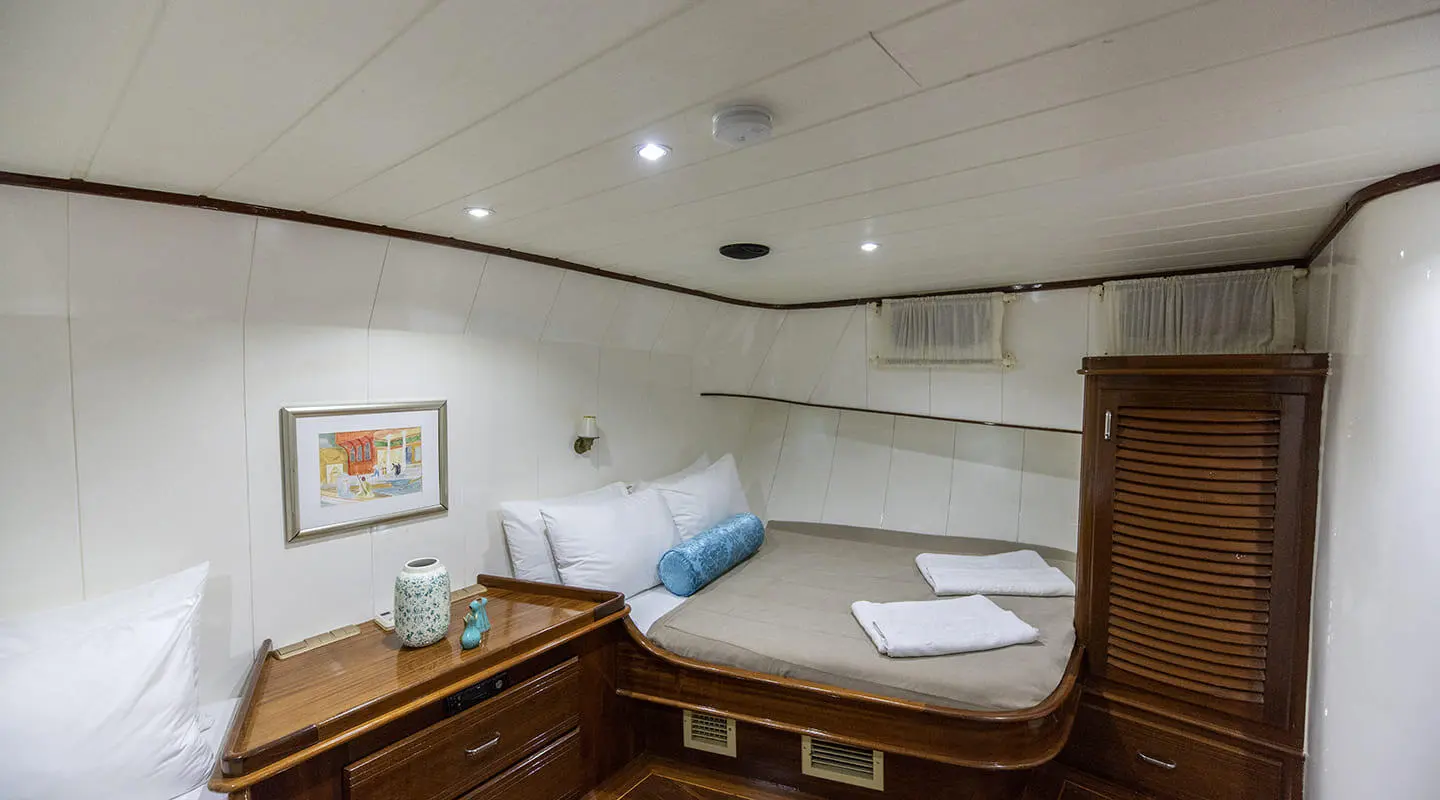 Interior of a yacht cabin with wooden cabinets, bed, and folded towels