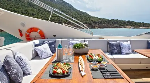 Onboard dining setup on Divine yacht with wooden table, plate of tapas, wine glass