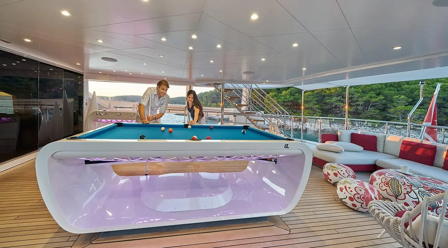 People on a luxury yacht deck near a purple-lit hot tub with string lights