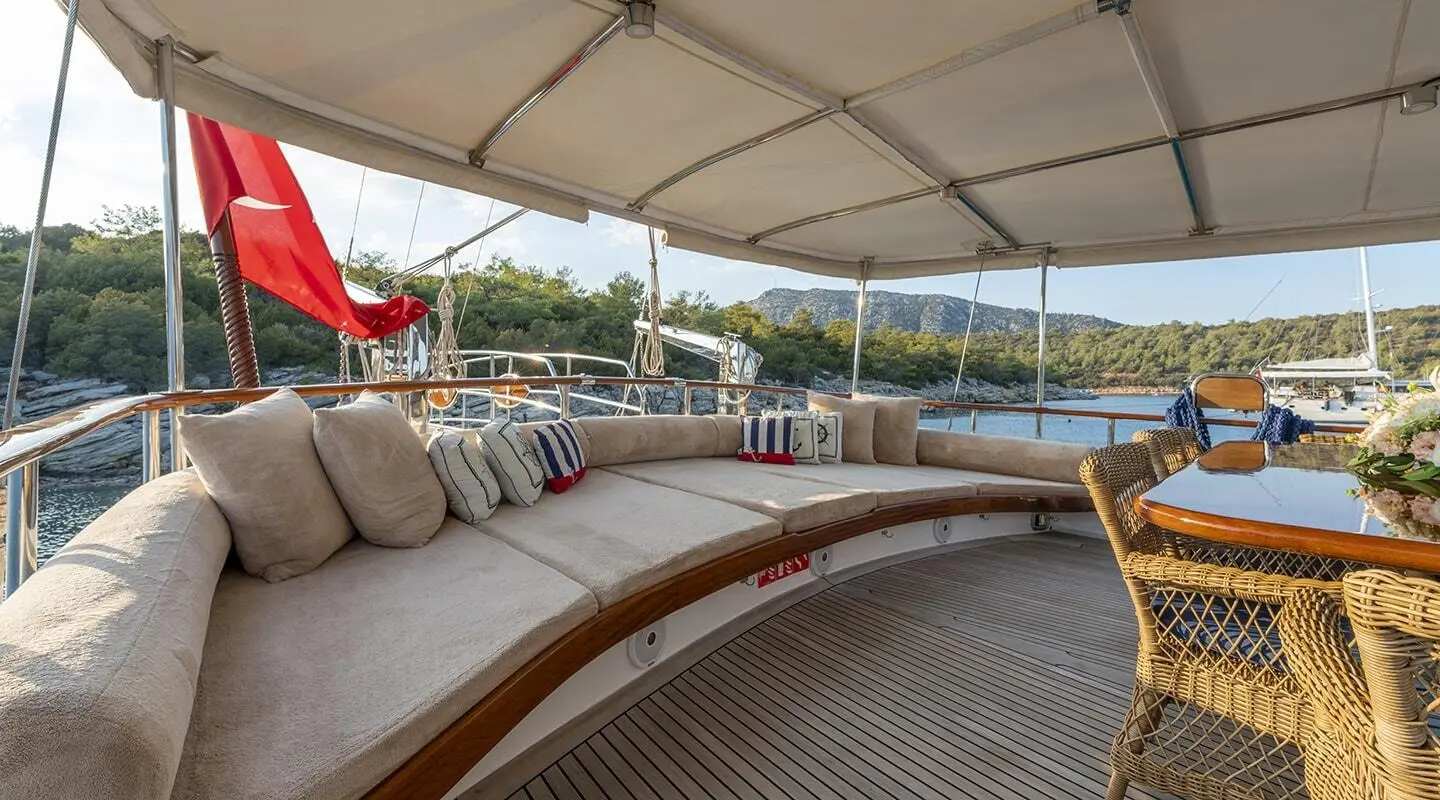 Artemis luxury yacht deck with wooden railings, cushioned seating, and sun loungers at sunset