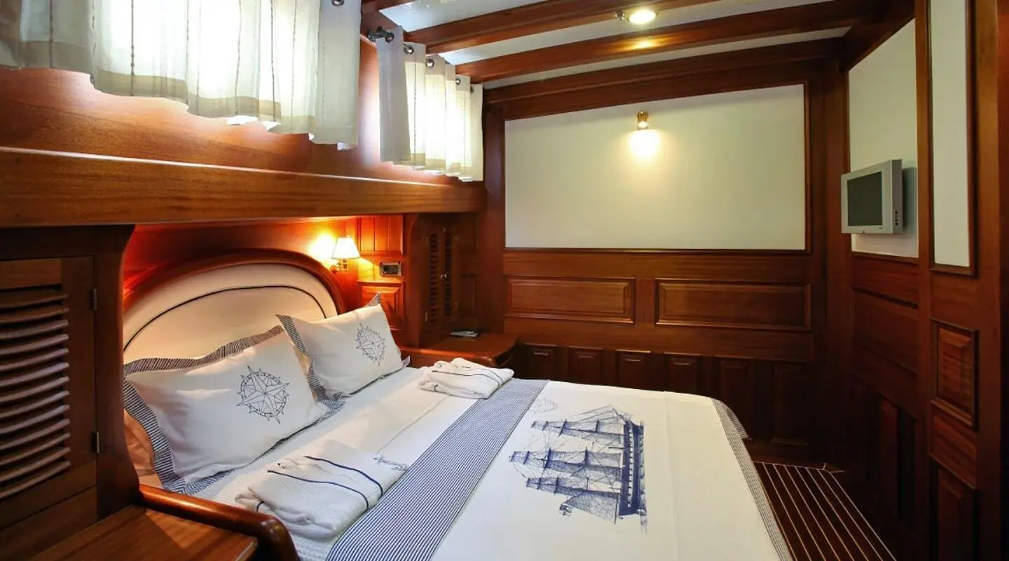 Interior view of Kaya Guneri 4 gulet showing wood cabin, bed, pillows, and porthole window
