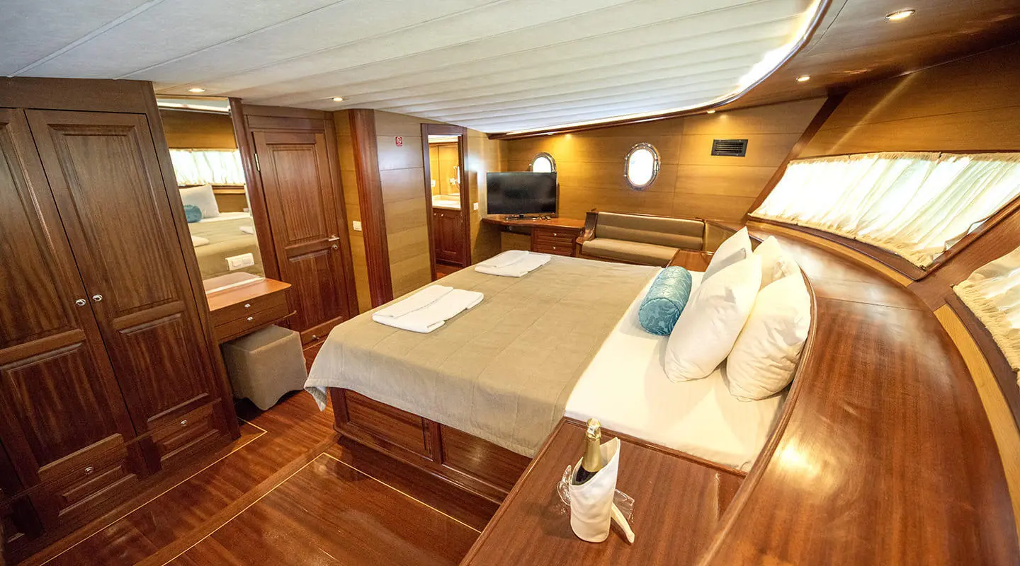 Kayhan 4 yacht interior with a large bed, warm wood tones, and seating