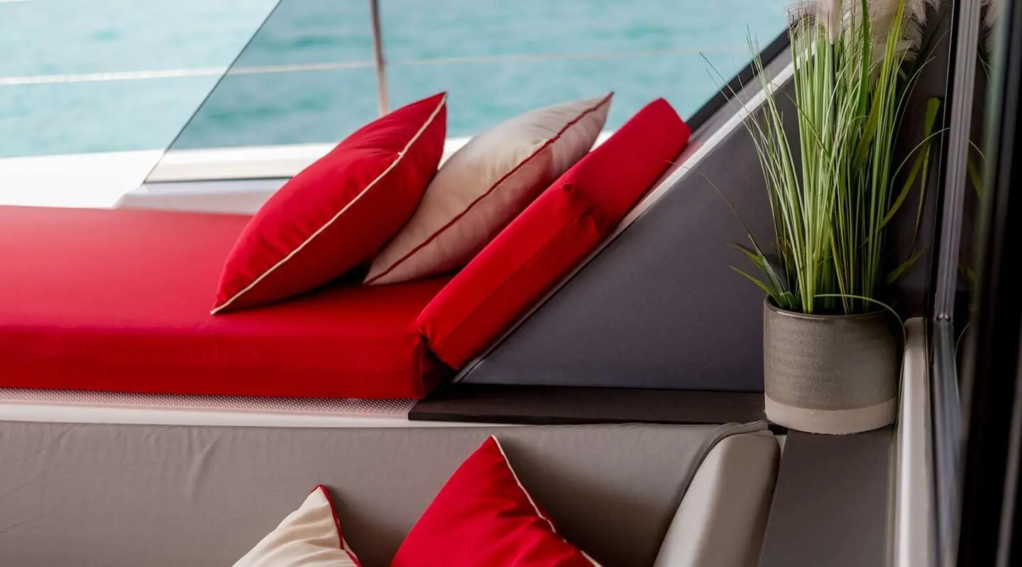 Red cushions on an open deck with a plant, overlooking the sea